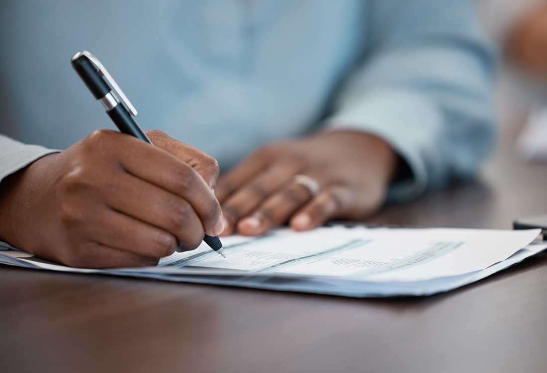Regulatory Compliance Advisory - man signing paperwork at a table or desk in the office